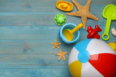 Beach ball and sand toys on light blue wooden background, flat lay. Space for text