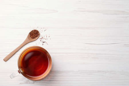 Freshly brewed rooibos tea, dry leaves and spoon on white wooden table, flat lay. Space for textの写真素材