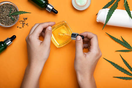 Woman dripping hemp oil into bowl on orange background, top view. Natural cosmeticsの写真素材