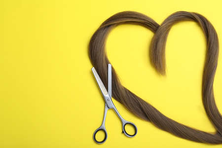 Professional hairdresser scissors, hair strands and space for text on yellow background, flat lay....
