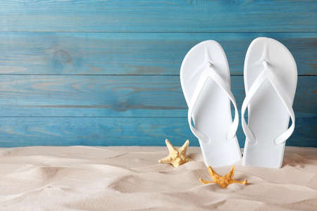 Stylish flip flops and starfish on sand near blue wooden wall, space for textの写真素材
