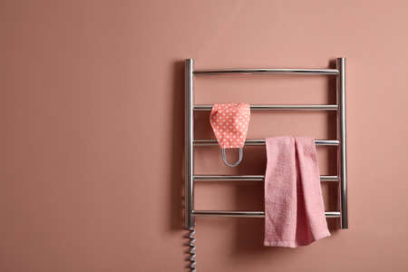 Modern heated towel rail with cloth face mask and towel on light pink wall. Space for textの写真素材