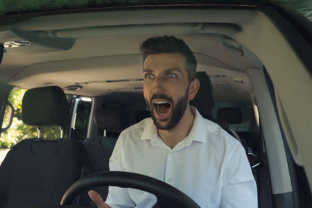 Stressed angry man in driver's seat of modern car, view through windshield