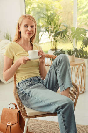 Woman with cup sitting in armchair at indoor terraceの写真素材