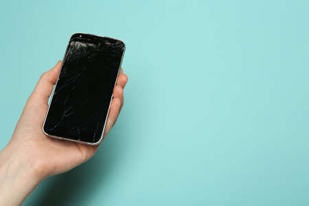 Woman holding damaged smartphone on light blue background, closeup with space for text. Device...