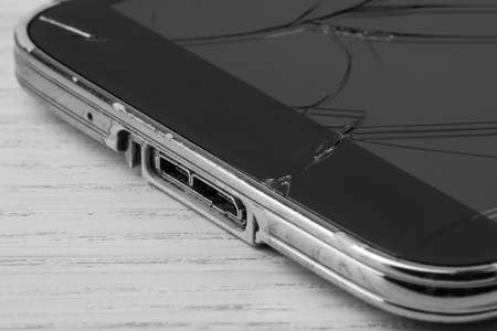 Smartphone with cracked screen on light beige wooden background, closeup. Device repair