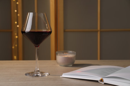 Glass of red wine, open book and candle on wooden table indoors, space for textの写真素材