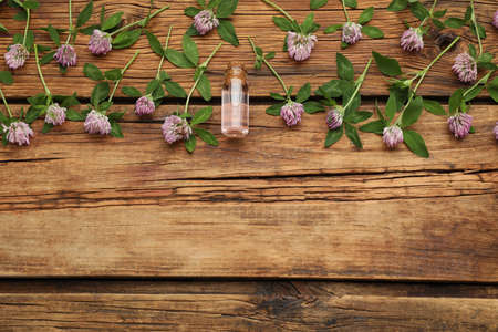 Beautiful clover flowers and bottle of essential oil on wooden table, flat lay. Space for textの写真素材