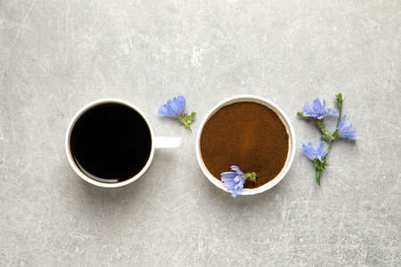 Cup of delicious chicory drink, powder and flowers on light gray table, flat layの写真素材