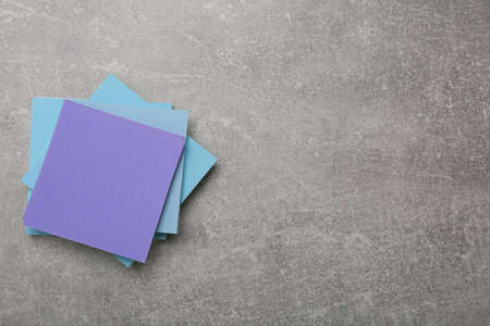 Stack of colorful stickers on light gray stone table, top view. Space for text