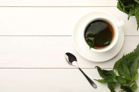 Cup of aromatic nettle tea and green leaves on white wooden table, flat lay. Space for textの写真素材