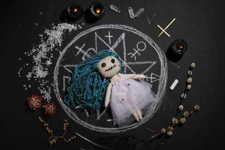 Female voodoo doll with pins surrounded by ceremonial items on black background, flat layの写真素材