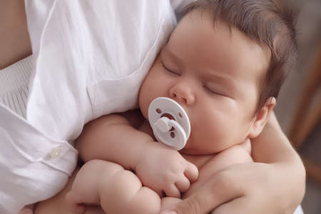 Mother holding her cute little baby with pacifier on blurred background, closeupの写真素材