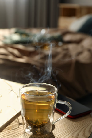 Glass cup of freshly brewed tea on wooden table in bedroom. Cozy home atmosphereの写真素材