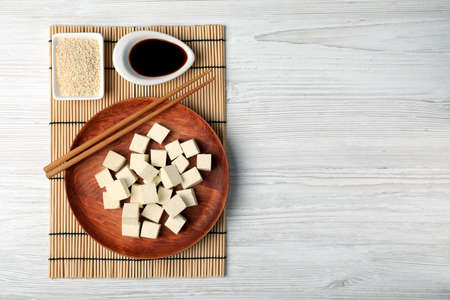 Delicious tofu with soy sauce and sesame seeds on white wooden table, flat lay. Space for text