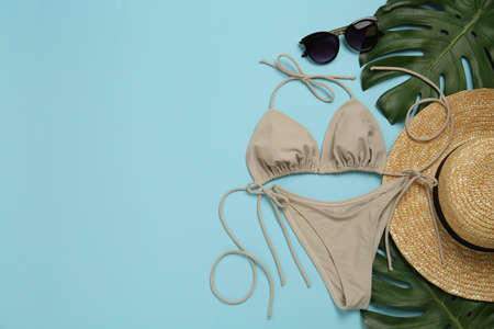 Stylish bikini, straw hat, sunglasses and tropical leaves on light blue background, flat lay. Space for textの写真素材