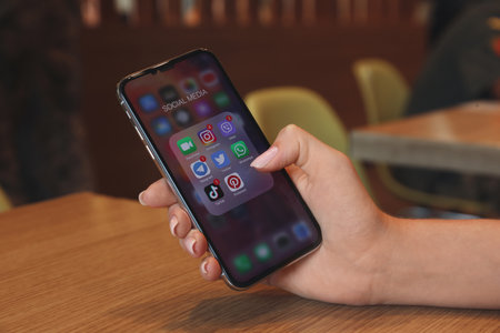 MYKOLAIV, UKRAINE - AUGUST 11, 2021: Woman using Apple iPhone X at wooden table, closeup. Screen with different social media iconsのeditorial素材