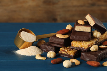 Different tasty bars, nuts and scoop of protein powder on blue wooden tableの写真素材