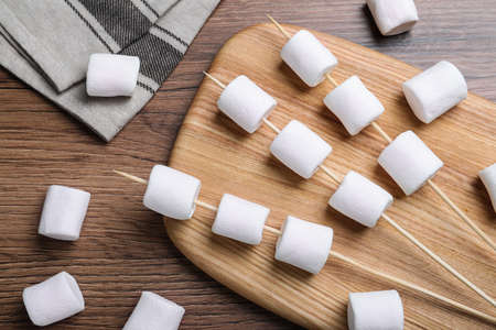 Sticks with delicious puffy marshmallows on wooden table, flat layの写真素材