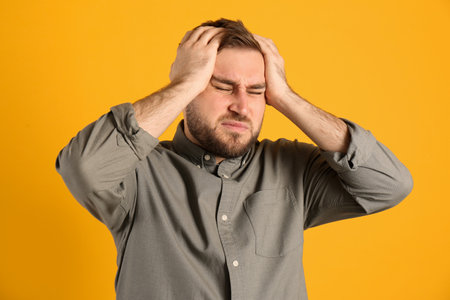 Man suffering from migraine on yellow backgroundの写真素材