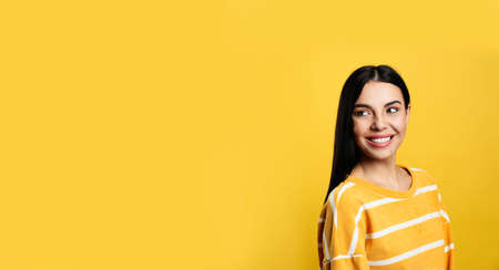 Portrait of happy young woman with beautiful black hair and charming smile on yellow background,...