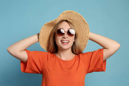 Beautiful young woman wearing straw hat and sunglasses on light blue background. Stylish headdressの写真素材
