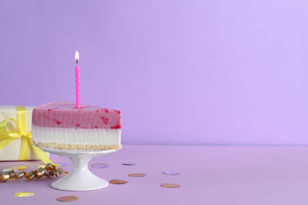 Piece of delicious birthday cake with candle near gift box on violet background, space for textの写真素材