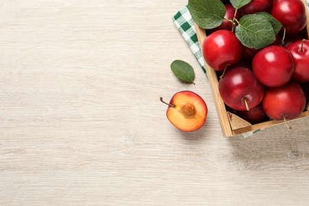 Delicious ripe cherry plums with leaves on white wooden table, flat lay. Space for text