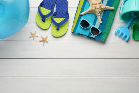 Flat lay composition with beach ball, plastic toys and accessories on white wooden background. Space...