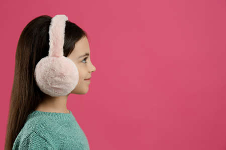 Cute little girl wearing stylish earmuffs on pink background. Space for textの写真素材
