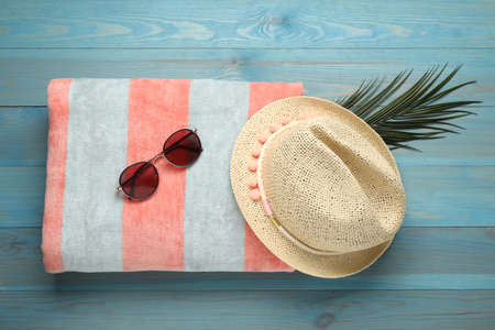Beach towel, straw hat and sunglasses on light blue wooden background, flat layの写真素材