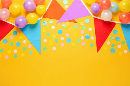 Bunting with colorful triangular flags and other festive decor on yellow background, flat lay. Space...