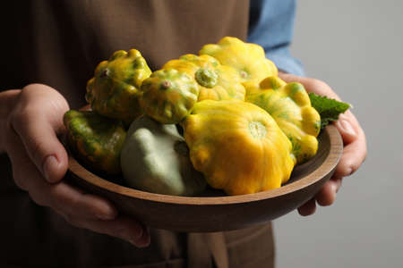Woman with wooden bowl of fresh ripe pattypan squashes on gray background, closeupの写真素材
