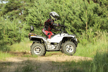 Man driving modern quad bike on sandy road near forest. Extreme sport