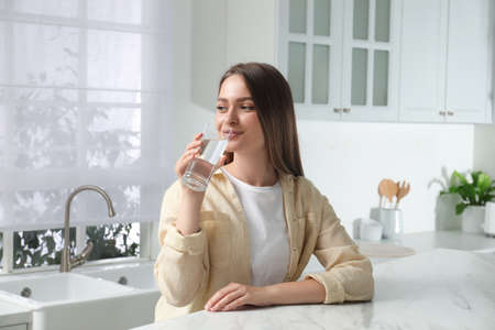 Woman drinking tap water from glass in kitchenの写真素材