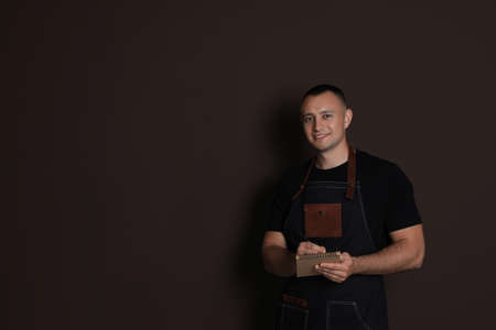 Portrait of happy young waiter with notebook on brown background, space for textの写真素材