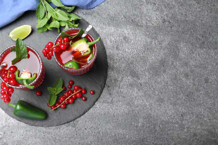 Glasses of spicy red currant cocktail with jalapeno and mint on gray table, flat lay. Space for textの写真素材