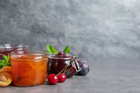 Jars with different jams and fresh fruits on gray table. Space for textの写真素材