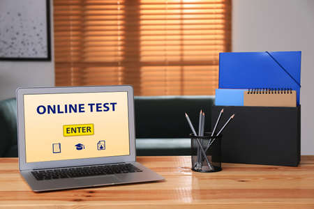 Laptop with online test and stationery on table in officeの写真素材