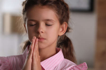 Cute little girl with hands clasped together praying at homeの写真素材