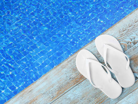 Pair of flip flops on wooden deck near swimming pool, top viewの写真素材