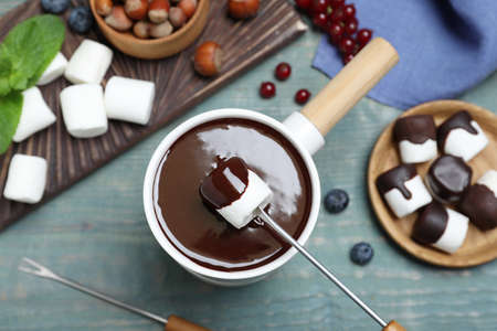 Dipping marshmallow into melted chocolate at blue wooden table, flat layの写真素材