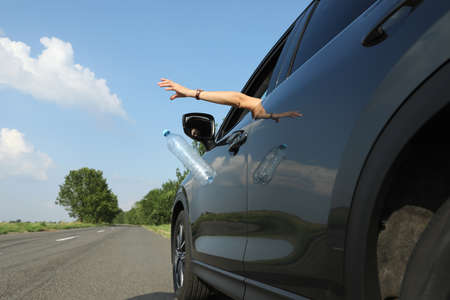 Driver throwing away plastic bottle from car window. Garbage on roadの写真素材