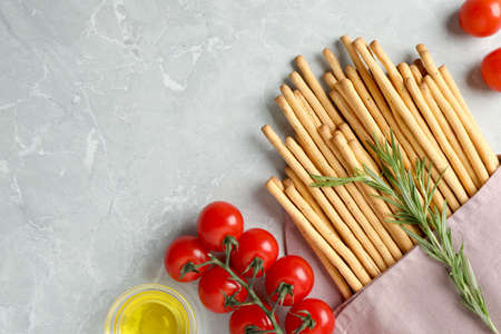 Delicious grissini sticks, oil, rosemary and tomatoes on gray marble table, flat lay. Space for textの写真素材