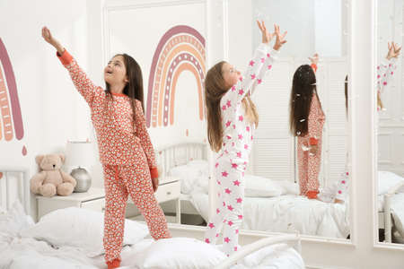 Cute little girls in pajamas playing with feathers on bed at home. Happy childhoodの写真素材
