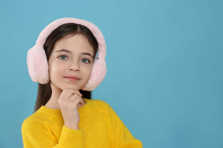 Cute little girl wearing stylish earmuffs on light blue background. Space for text