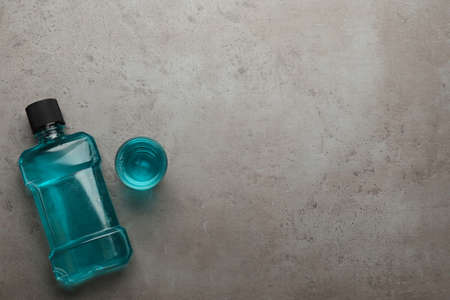 Bottle and glass with mouthwash on gray table, flat lay. Space for textの写真素材
