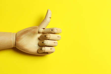 Wooden mannequin hand showing thumb up on yellow background, top view. Space for textの写真素材