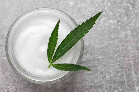 Jar of hemp cream and leaf on gray table, top view. Natural cosmeticsの写真素材