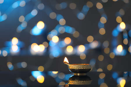 Lit diya on table against blurred lights, space for text. Diwali lamp